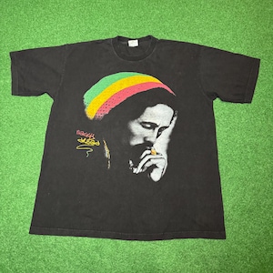 May include: Black t-shirt featuring a portrait of a man with a colorful hat. The image includes the text "Dread" in yellow and green. The man is depicted with a thoughtful expression, with his hand near his mouth.