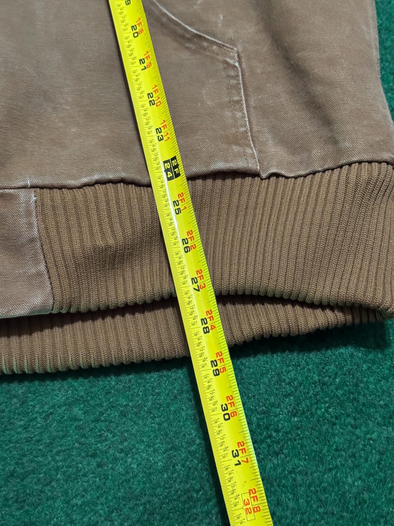 Puede incluir: Una sudadera con capucha marr&oacute;n con dobladillo inferior acanalado. Una cinta m&eacute;trica amarilla se coloca sobre la prenda, mostrando medidas de hasta 81 cm.