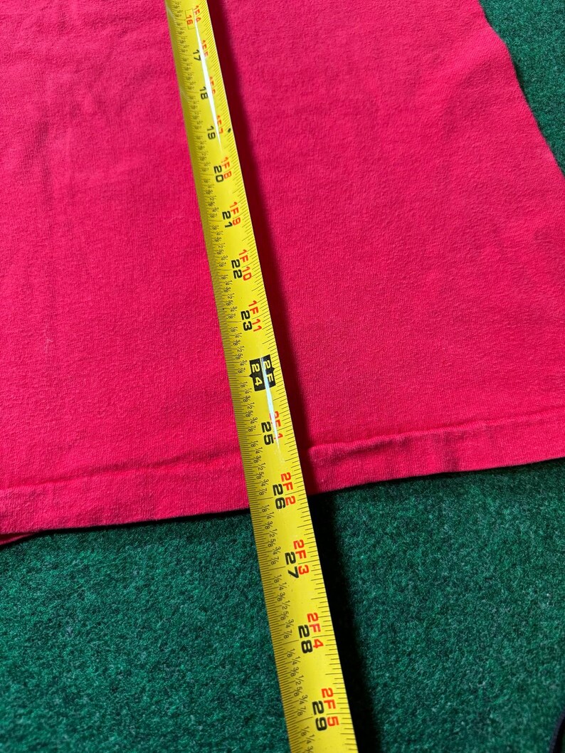May include: A close-up of a pink fabric with a yellow measuring tape. The tape measures 29 inches.