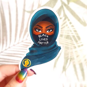 May include: A sticker featuring a woman wearing a blue hijab and a black face mask with the text "Black Lives Matter". The sticker also features a raised fist in a yellow circle.