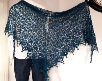 Puede incluir: Un chal de ganchillo azul turquesa con un delicado patrón de encaje. El chal está drapeado sobre una persona que lleva una camisa blanca y unos vaqueros azules.
