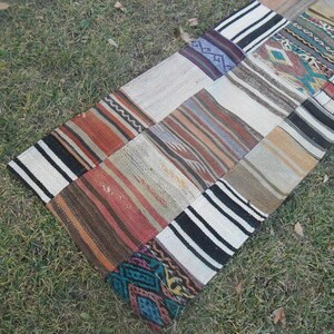 Puede incluir: Una alfombra de patchwork con una variedad de colores y patrones, incluyendo negro, blanco, marrón, rojo y azul. La alfombra está hecha de tejido tejido y tiene una forma rectangular.