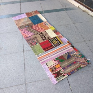 以下が含まれることがあります： 赤、青、緑、黄、ピンクなど、さまざまな色と模様が施された長方形の長いパッチワークの敷物。敷物はさまざまな生地と質感でできており、フリンジの縁があります。