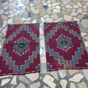 Puede incluir: Dos alfombras de color burdeos con intrincados patrones geom&eacute;tricos en tonos azules, verdes y rosas. Las alfombras tienen un borde con flecos y est&aacute;n colocadas sobre un suelo de piedra.