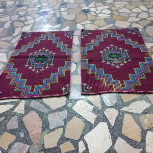 Puede incluir: Dos alfombras de oraci&oacute;n color burdeos con patrones geom&eacute;tricos en tonos de azul, verde, amarillo y rosa. Las alfombras est&aacute;n colocadas sobre un suelo de baldosas.