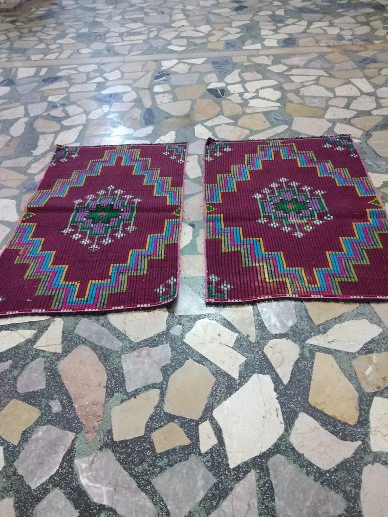 Puede incluir: Dos alfombras de oraci&oacute;n color burdeos con patrones geom&eacute;tricos en tonos de azul, verde, amarillo y rosa. Las alfombras est&aacute;n colocadas sobre un suelo de baldosas.