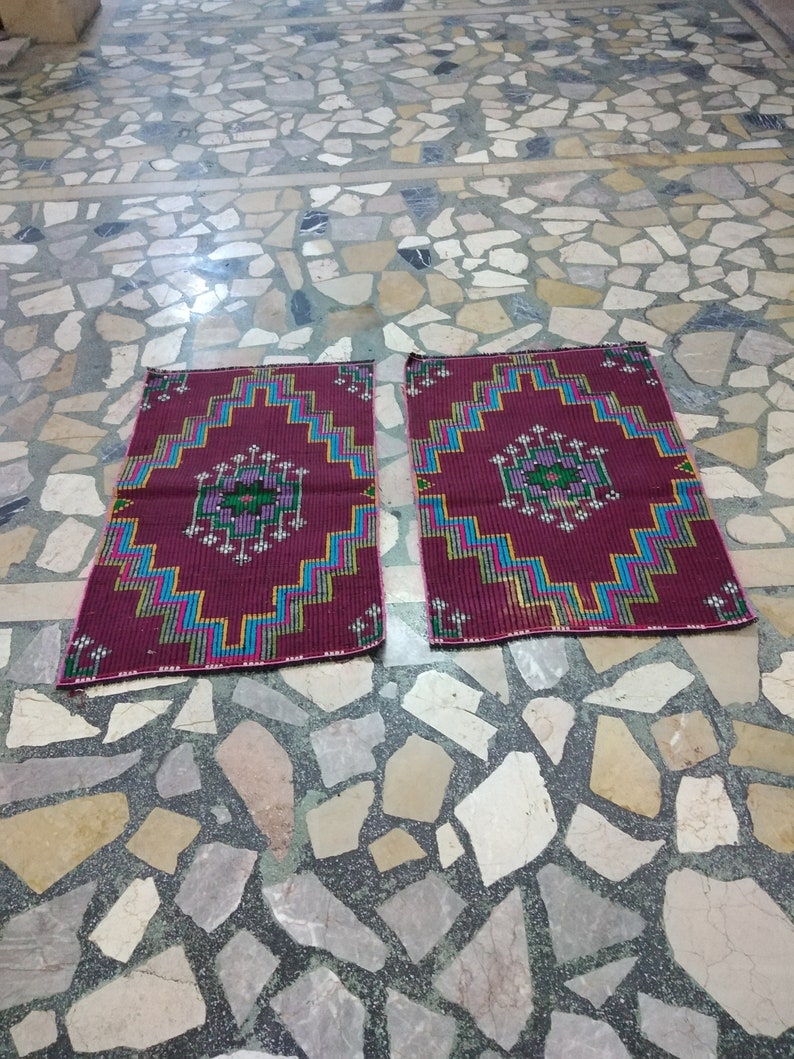 Puede incluir: Dos alfombras de oraci&oacute;n de color rojo, azul y verde con patrones sobre un suelo de baldosas.