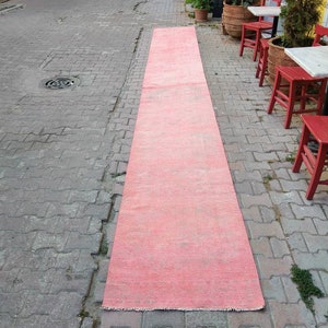 May include: A long, bright pink rug laid out on a gray brick walkway. The rug is slightly faded and has a frayed edge.