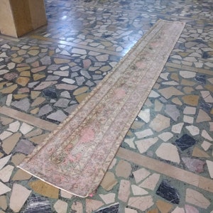 Puede incluir: Una alfombra larga y estrecha de color rosa y crema con un patrón floral. La alfombra está sobre un suelo de baldosas.