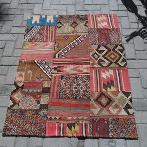 Peut inclure: Un tapis patchwork coloré avec une variété de motifs géométriques dans des tons de rouge, marron, bleu et blanc.
