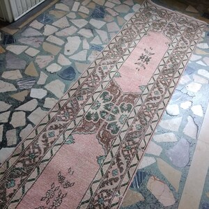 May include: A pink and brown patterned runner rug with a floral design. The rug is laid on a floor made of small, irregular shaped tiles.