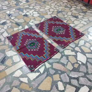 Puede incluir: Dos alfombras de colores con dise&ntilde;os geom&eacute;tricos en tonos rojos, rosas, azules, verdes y blancos. Las alfombras est&aacute;n colocadas sobre un suelo de piedra.