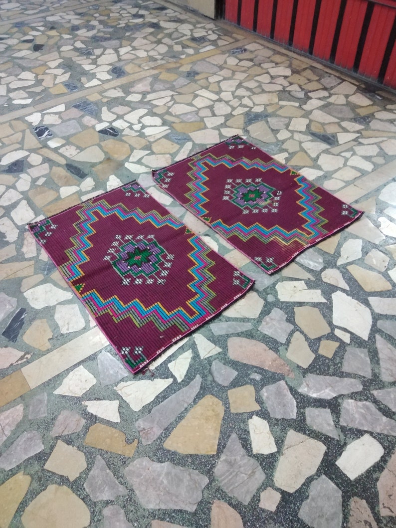 Puede incluir: Dos alfombras de colores con dise&ntilde;os geom&eacute;tricos en tonos rojos, rosas, azules, verdes y blancos. Las alfombras est&aacute;n colocadas sobre un suelo de piedra.