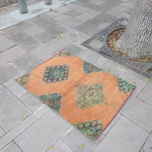 May include: A vintage orange and green patterned rug with a diamond design. The rug is lying on a grey concrete surface.