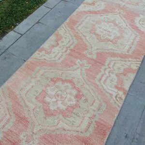 May include: A long, narrow rug with a pink and cream color scheme. The rug has a traditional Persian design with intricate patterns and a faded, vintage look.
