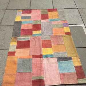 Puede incluir: Una alfombra de patchwork con una variedad de colores y texturas, incluyendo rojo, naranja, amarillo, verde, azul y gris. La alfombra está hecha de tejido tejido y tiene una forma rectangular.