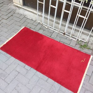 Może przedstawiać: Czerwony dywan z frędzlami. Dywan leży na szarej powierzchni z cegły.