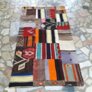 Może przedstawiać: Kolorowy dywan patchworkowy z różnymi geometrycznymi wzorami i kolorami, w tym czerwony, niebieski, zielony i brązowy.