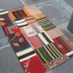Puede incluir: Una alfombra de patchwork colorida con una variedad de patrones y colores, incluyendo rojo, naranja, amarillo, verde, azul y marrón. La alfombra está hecha de tejido tejido y tiene un borde con flecos.