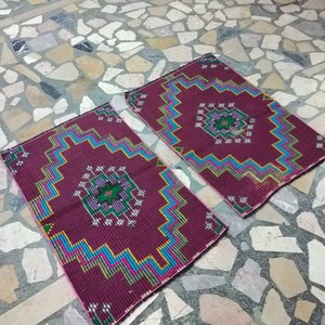 Puede incluir: Dos alfombras de color burdeos con dise&ntilde;os geom&eacute;tricos en tonos azules, verdes, amarillos y rosas. Las alfombras est&aacute;n colocadas sobre un suelo de piedra.