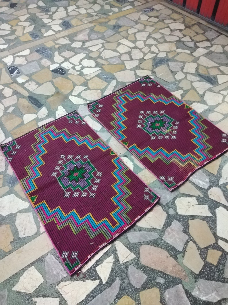 Puede incluir: Dos alfombras de color burdeos con dise&ntilde;os geom&eacute;tricos en tonos azules, verdes, amarillos y rosas. Las alfombras est&aacute;n colocadas sobre un suelo de piedra.