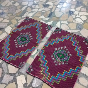 Puede incluir: Dos alfombras de color burdeos con patrones geom&eacute;tricos en tonos de azul, verde, rosa y amarillo. Las alfombras est&aacute;n sobre un suelo de baldosas.