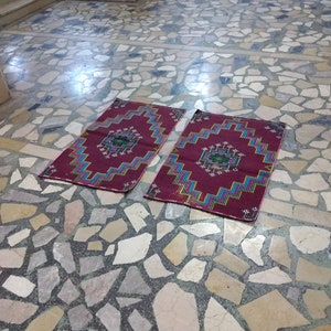 Puede incluir: Dos alfombras de oraci&oacute;n coloridas con patrones geom&eacute;tricos en tonos rojos, azules, verdes y amarillos, colocadas sobre un suelo de piedra.
