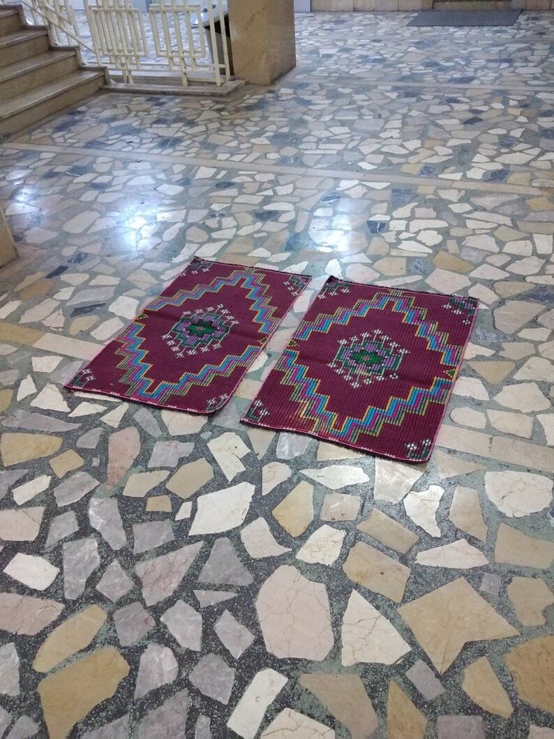 Puede incluir: Dos alfombras de oraci&oacute;n coloridas con patrones geom&eacute;tricos en tonos rojos, azules, verdes y amarillos, colocadas sobre un suelo de piedra.