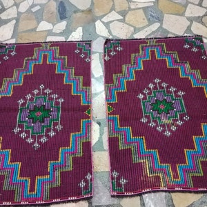 Puede incluir: Dos alfombras color burdeos con patrones geom&eacute;tricos en tonos azules, verdes, amarillos y rosas. Las alfombras tienen un borde con flecos.