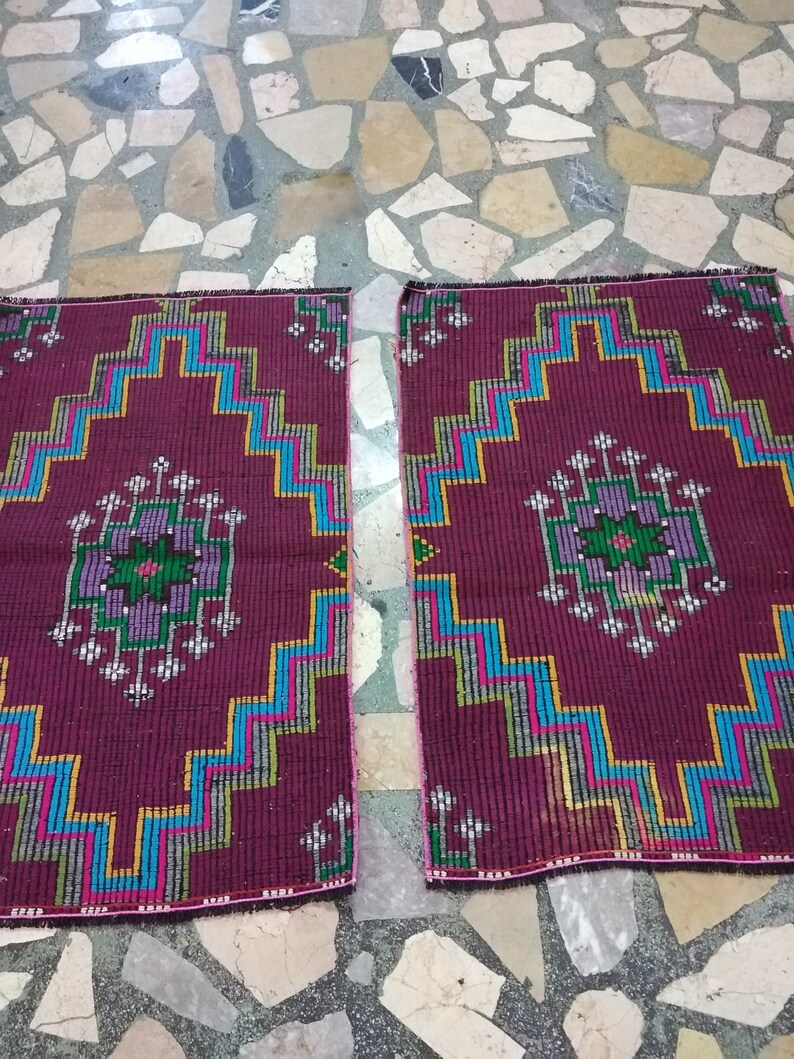 Puede incluir: Dos alfombras color burdeos con patrones geom&eacute;tricos en tonos azules, verdes, amarillos y rosas. Las alfombras tienen un borde con flecos.