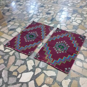 Puede incluir: Dos alfombras de oraci&oacute;n con patrones, con fondo burdeos y dise&ntilde;os geom&eacute;tricos coloridos. Las alfombras est&aacute;n colocadas sobre un suelo de baldosas.