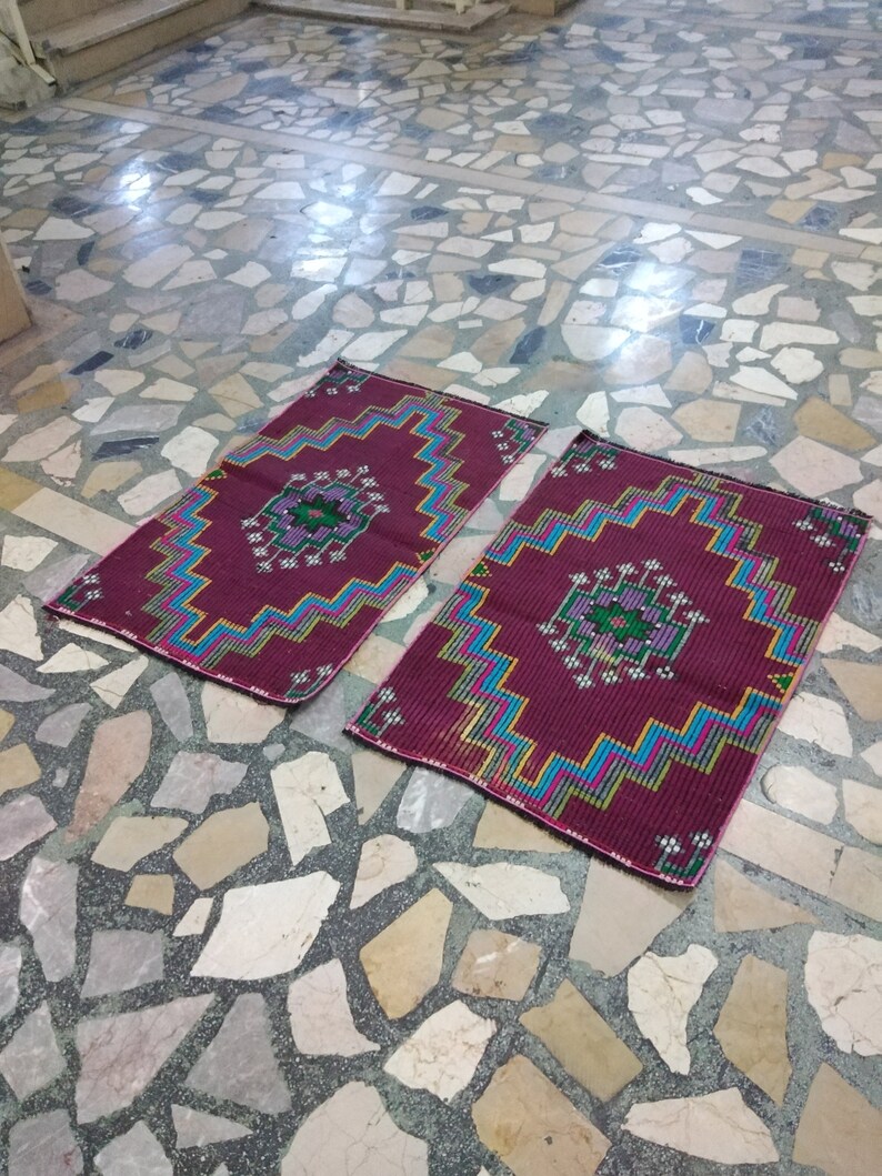 Puede incluir: Dos alfombras de oraci&oacute;n con patrones, con fondo burdeos y dise&ntilde;os geom&eacute;tricos coloridos. Las alfombras est&aacute;n colocadas sobre un suelo de baldosas.