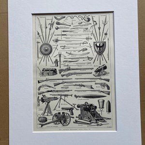 May include: Black and white print of various antique weapons, including swords, guns, and cannons, arranged in a detailed illustration. The print is framed in a white mat, showcasing a historical collection of armaments.