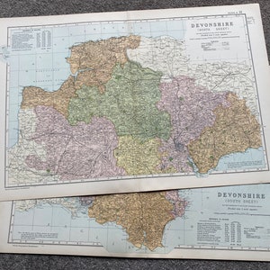 May include: Two vintage maps of Devonshire, England, with detailed cartography. The maps, labeled "Devonshire (South Sheet)", feature a color palette of greens, yellows, and pinks, with text and grid lines. The maps are on aged paper.