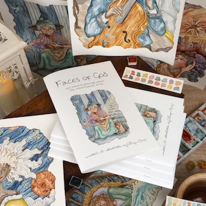 K&ouml;nnte beinhalten: Ein Buch mit dem Titel "Faces of God" mit Aquarell-Illustrationen. Der Buchumschlag zeigt eine Frau in einem blauen Kleid, die auf einem Stuhl sitzt und einen Vogel auf ihrer Hand hat. Das Buch ist von anderen Aquarell-Illustrationen umgeben.