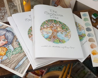 Könnte beinhalten: Ein Stapel kleiner, weißer Taschenbücher mit dem Titel "The Mandolina Tree" auf dem Cover. Das Cover zeigt eine Aquarellillustration eines Baumes mit einer Tür in seinem Stamm. Die Bücher liegen auf einer Holzoberfläche mit Aquarellfarben und Pinseln.
