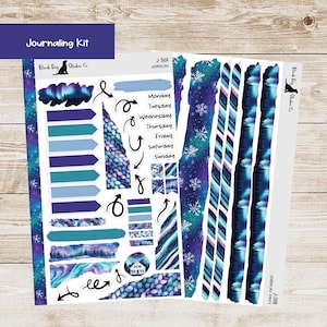 May include: A journaling kit with stickers featuring a winter theme. The kit includes stickers with arrows, labels, and decorative strips in shades of blue, purple, and teal. The text "Journaling Kit" is at the top.