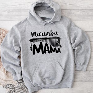 Może przedstawiać: Szara bluza z kapturem z czarnym nadrukiem marimby i tekstem "Marimba Mama".