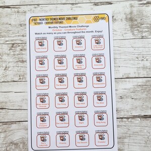 May include: A printable October movie challenge featuring a list of creature feature movies. The list is organized in a grid with each movie title in a square with a popcorn bucket icon. The title of the challenge is "Monthly Themed Movie Challenge" and "October - Creature Features".