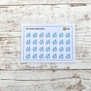 May include: A white sticker sheet with a dotted border and the text "BOTTLED BITS: MUSIC NOTES". The sheet is covered in light blue musical notes. A small bee graphic is in the upper right corner.