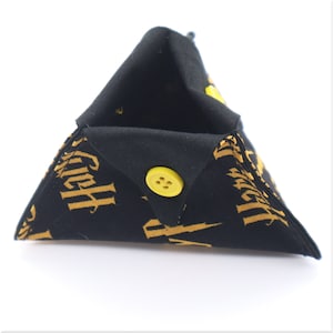 May include: Black triangular dice bag with a yellow button closure. The bag is made of fabric with a repeating pattern of gold lettering on a black background.