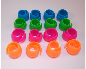 May include: A set of 15 colorful plastic yarn holders in various shades of blue, green, pink, and orange. The holders are designed to hold yarn in place while crocheting or knitting.