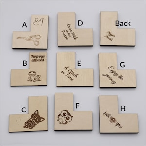 May include: A collection of nine wooden, L-shaped craft pieces. Each piece features engraved designs and text, including scissors, a frog, a cat, an owl, and phrases like "Cross Stitch is my Passion" and "Enjoy the journey."