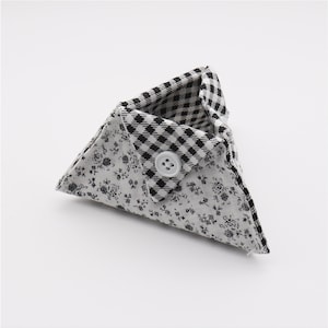 May include: A small, triangular fabric pouch with a button closure. The pouch features a floral pattern on the exterior and a black and white checkered pattern on the interior. The button is white.