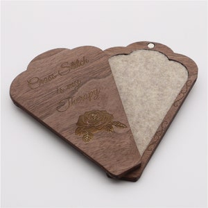 May include: A wooden box with a hinged lid, engraved with the text "Cross Stitch is really Therapy" and a rose design. The box is lined with a light brown felt material.