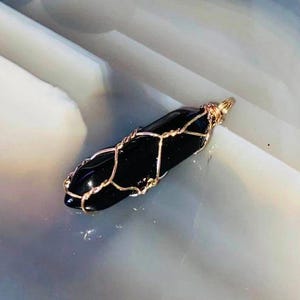 May include: A black gemstone pendant wrapped in gold wire. The pendant is shaped like a long, thin point.