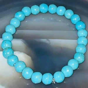 May include: A turquoise beaded bracelet. The bracelet features round, light blue beads with delicate veining. The beads are strung together, forming a circular shape, designed to be worn on the wrist. A bright and colourful accessory.