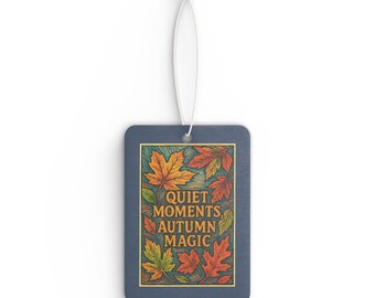 Könnte beinhalten: Ein rechteckiger Lufterfrischer mit dunkelblauem Rand und weißer Aufhängeschnur. Die Mitte zeigt eine farbenfrohe Illustration von Herbstblättern in Orange-, Rot- und Gelbtönen mit dem Text "QUIET MOMENTS, AUTUMN MAGIC" in Gold.