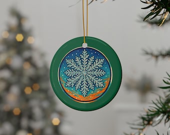 Könnte beinhalten: Ein runder, grüner Weihnachtsschmuck mit einem detaillierten Schneeflocken-Design. Die Schneeflocke ist hellblau und vor einem blauen Hintergrund mit goldenen Akzenten platziert. Der Schmuck hängt an einem goldenen Faden, ideal für die Weihnachtsdekoration.