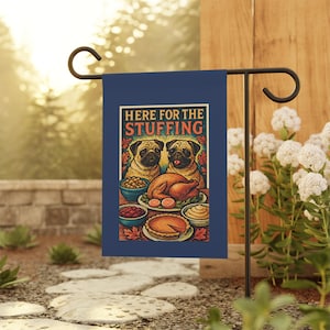 Op de afbeelding: Een marineblauwe tuinvaandel met een Thanksgiving-illustratie. Het toont twee mopshonden, een gebraden kalkoen, bijgerechten en de tekst "HERE FOR THE STUFFING". De vlag staat op een zwarte metalen standaard in een tuin.